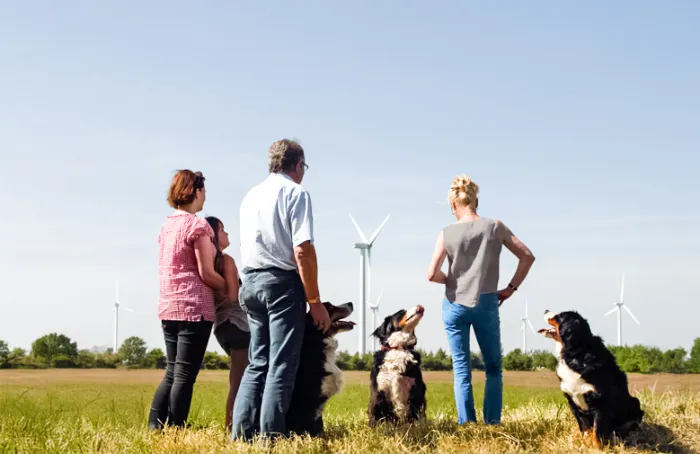Leute mit Hunden auf Wiese mit Windrad im Hintergrund